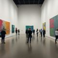 Oameni admirând picturi abstracte colorate într-o galerie de artă.